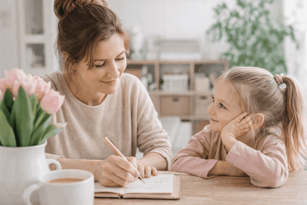 Mutter plant am Tisch mit Notizbuch, während ihr Kind daneben sitzt – Mental Load im Familienalltag sichtbar machen